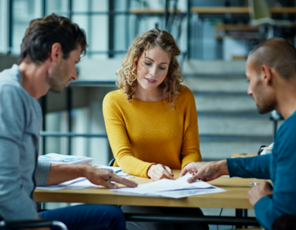 Three persons in an office pointing and reading a paper